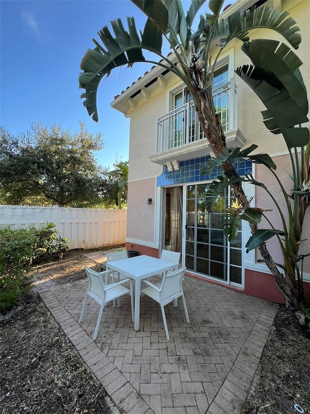 view of patio with outdoor dining area, fence, and a balcony