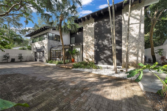 view of front facade featuring a garage, stone siding, fence, and decorative driveway