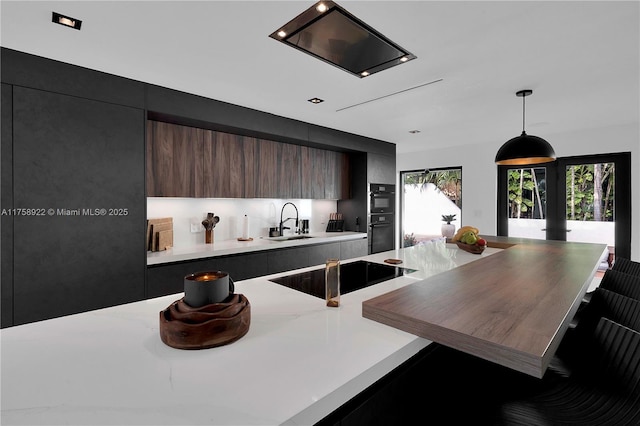 kitchen featuring dobule oven black, modern cabinets, decorative light fixtures, light countertops, and a sink