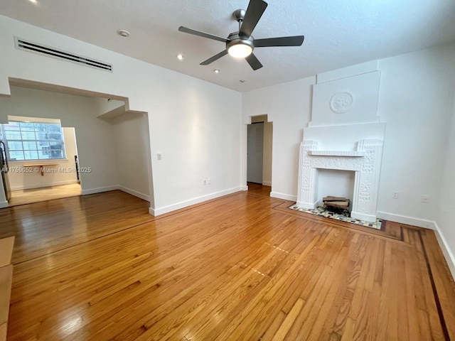 unfurnished living room featuring a fireplace with flush hearth, visible vents, a ceiling fan, baseboards, and wood-type flooring