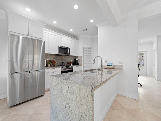 kitchen with a peninsula, a sink, appliances with stainless steel finishes, tasteful backsplash, and crown molding