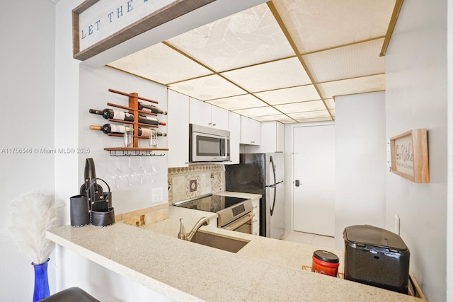 kitchen with a peninsula, a sink, stainless steel appliances, white cabinetry, and backsplash