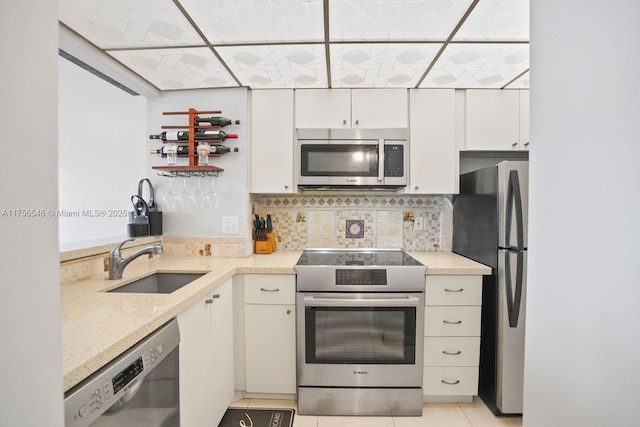 kitchen with stainless steel appliances, a sink, white cabinetry, light stone countertops, and tasteful backsplash