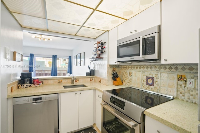 kitchen featuring decorative backsplash, appliances with stainless steel finishes, white cabinets, a sink, and a peninsula