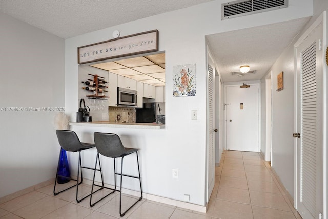 kitchen with light tile patterned floors, visible vents, stainless steel microwave, freestanding refrigerator, and a kitchen bar