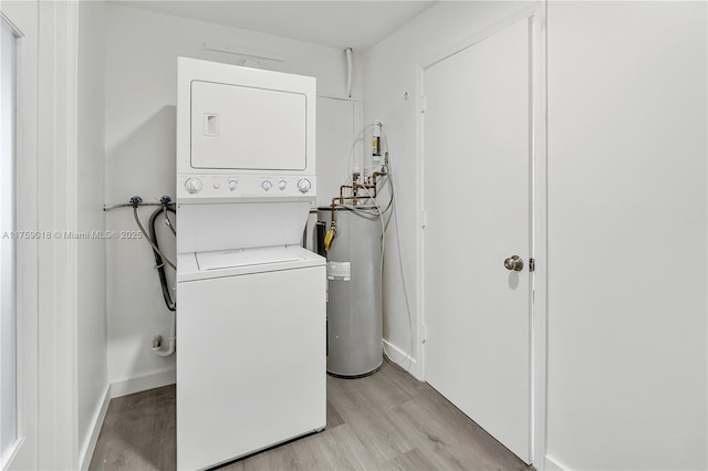 clothes washing area with electric water heater, laundry area, baseboards, light wood finished floors, and stacked washer and clothes dryer