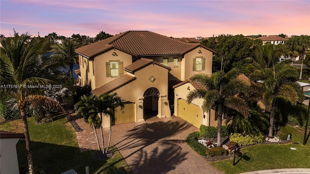 mediterranean / spanish-style home with an attached garage, stucco siding, a front lawn, a tile roof, and decorative driveway