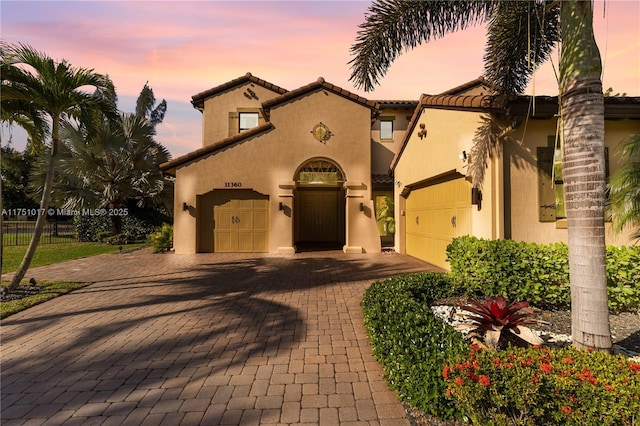 mediterranean / spanish home with stucco siding, decorative driveway, an attached garage, and a tile roof