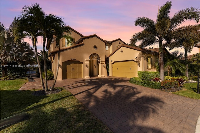 mediterranean / spanish house with a front lawn, a tile roof, stucco siding, decorative driveway, and a garage