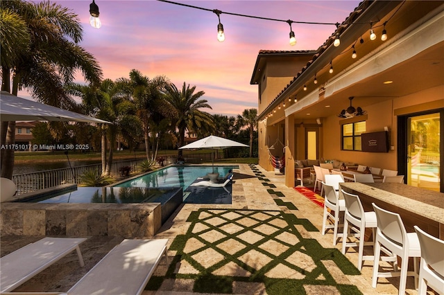 11360 NW 83rd Way, Parkland, FL 33076 - pool at dusk featuring a fenced in pool, an outdoor bar, fence, a patio, and an outdoor living space