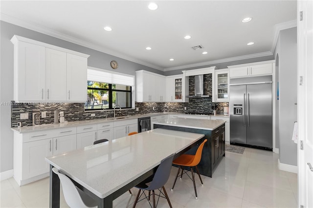 kitchen with a center island, crown molding, wall chimney range hood, built in refrigerator, and a sink