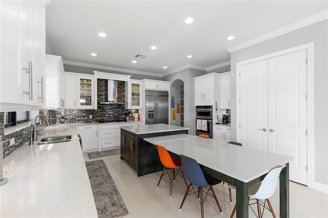 kitchen with a sink, a large island, wall chimney exhaust hood, multiple ovens, and stainless steel built in refrigerator