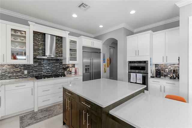 kitchen with visible vents, stainless steel appliances, crown molding, wall chimney range hood, and glass insert cabinets