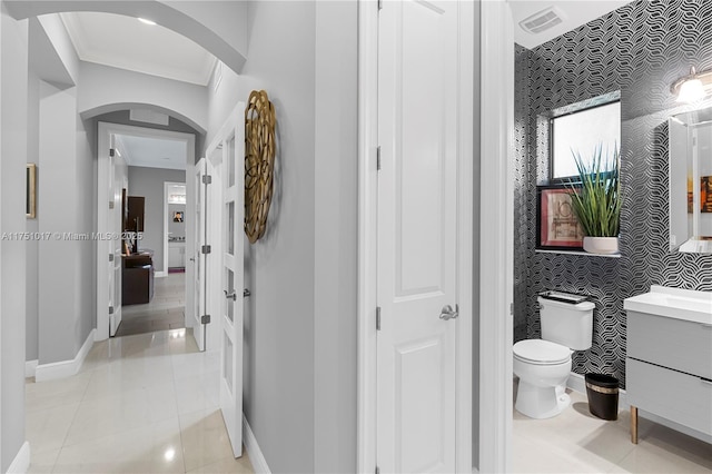 bathroom featuring vanity, baseboards, wallpapered walls, an accent wall, and toilet