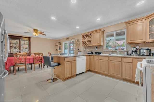 kitchen featuring light brown cabinets, a peninsula, white dishwasher, light countertops, and range