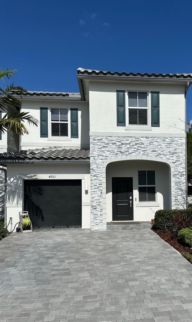 view of front of home with decorative driveway, a tile roof, stucco siding, an attached garage, and stone siding