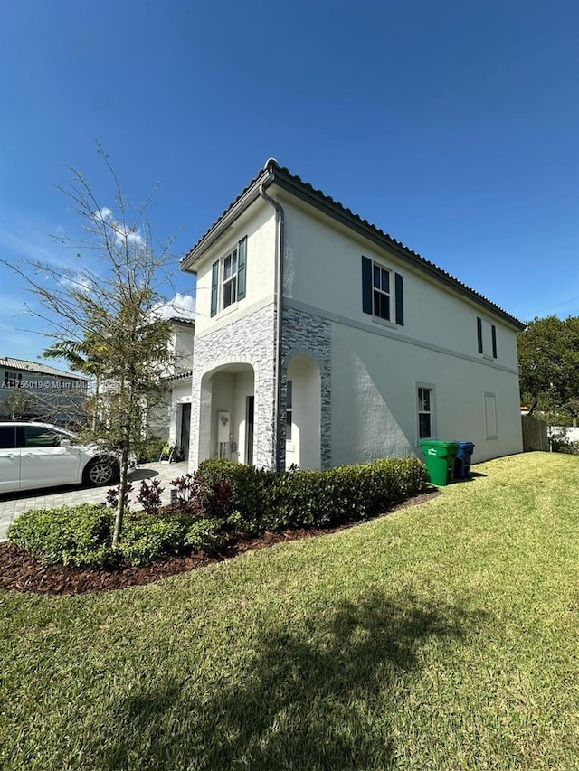 view of side of property with stone siding, a lawn, driveway, and stucco siding