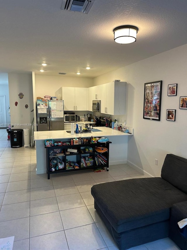 kitchen with light tile patterned flooring, a peninsula, visible vents, light countertops, and appliances with stainless steel finishes