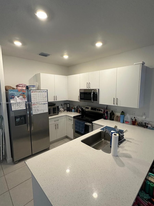 kitchen with light tile patterned floors, appliances with stainless steel finishes, white cabinets, a sink, and a peninsula