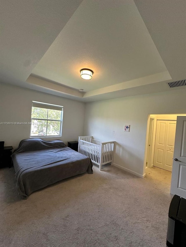 carpeted bedroom featuring a tray ceiling, visible vents, and baseboards