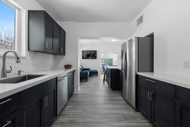 kitchen featuring stainless steel appliances, light countertops, light wood-style floors, a sink, and dark cabinetry