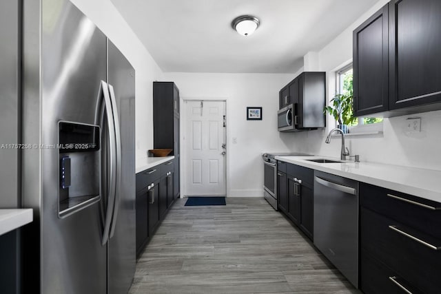 kitchen with dark cabinets, stainless steel appliances, a sink, light wood-style floors, and light countertops