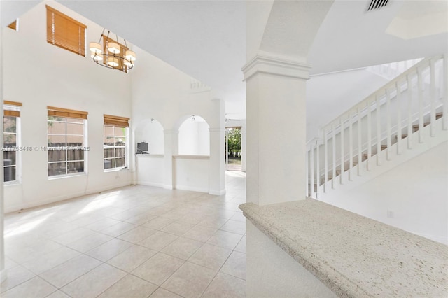 tiled entryway featuring decorative columns, baseboards, a high ceiling, stairs, and a chandelier