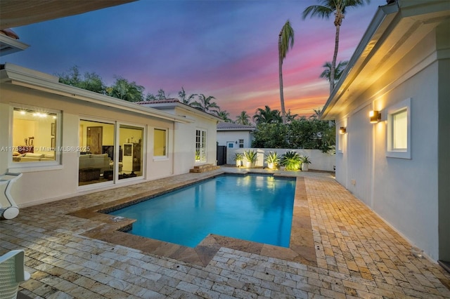 pool at dusk with a patio area, fence, and a fenced in pool