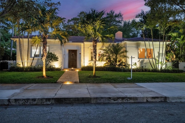 mediterranean / spanish home featuring stucco siding, a chimney, a tiled roof, and a yard