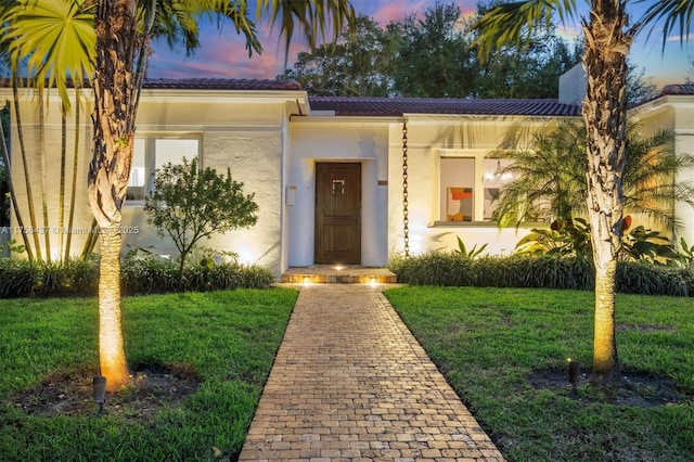 exterior entry at dusk featuring stucco siding and a yard