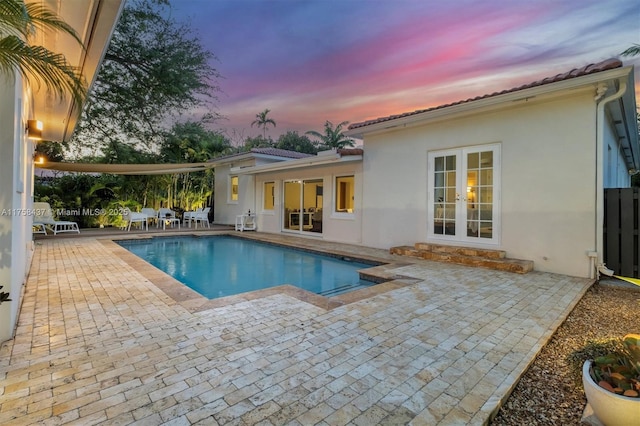 pool at dusk with an outdoor pool, entry steps, french doors, and a patio