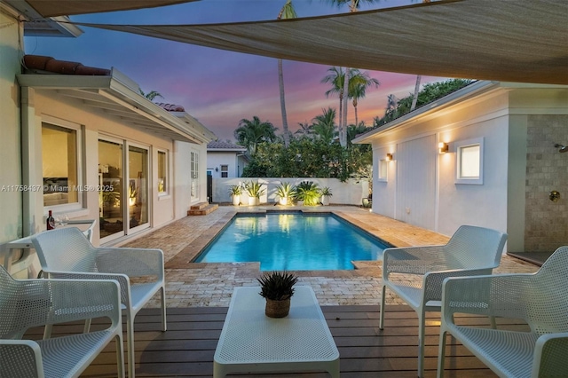 pool at dusk featuring a fenced backyard, a fenced in pool, and a wooden deck