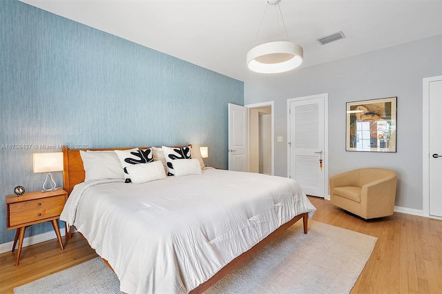 bedroom with wallpapered walls, an accent wall, light wood-type flooring, baseboards, and visible vents