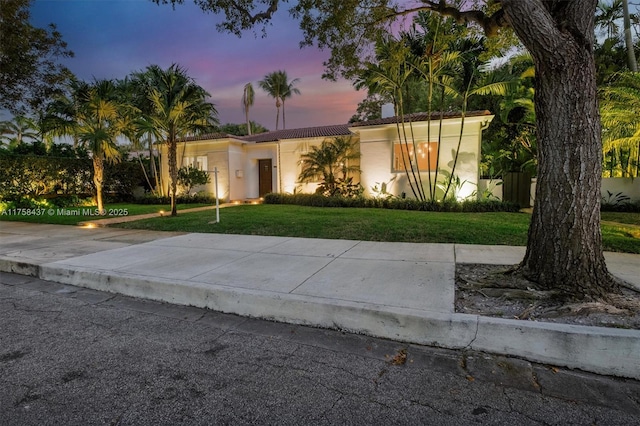 view of front of house featuring a lawn, a tiled roof, and stucco siding