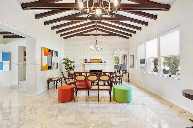 dining area with a chandelier, brick wall, a fireplace, marble finish floor, and beamed ceiling