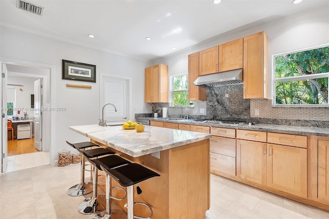 kitchen featuring stainless steel gas cooktop, visible vents, light brown cabinetry, a sink, and under cabinet range hood