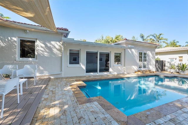 back of house with a deck, fence, a tile roof, an outdoor pool, and stucco siding