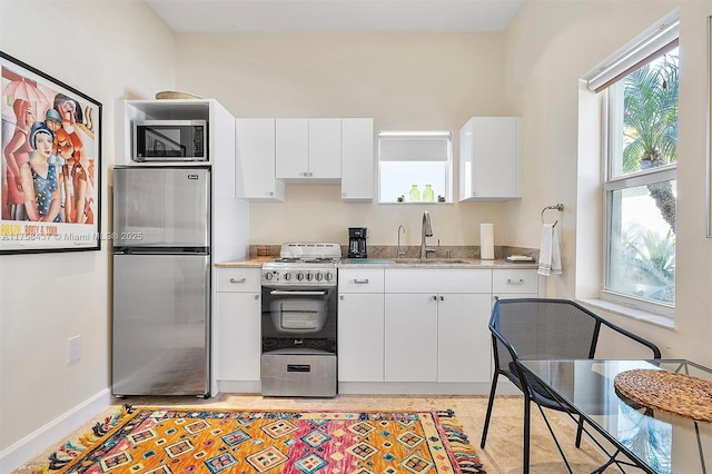 kitchen featuring appliances with stainless steel finishes, white cabinets, a sink, and baseboards