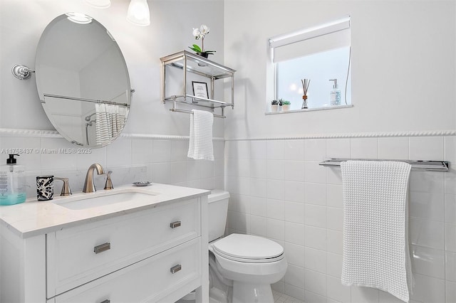 bathroom with toilet, wainscoting, tile walls, and vanity