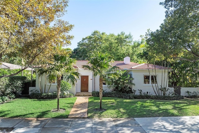 mediterranean / spanish house featuring a tile roof, a chimney, a front lawn, and stucco siding