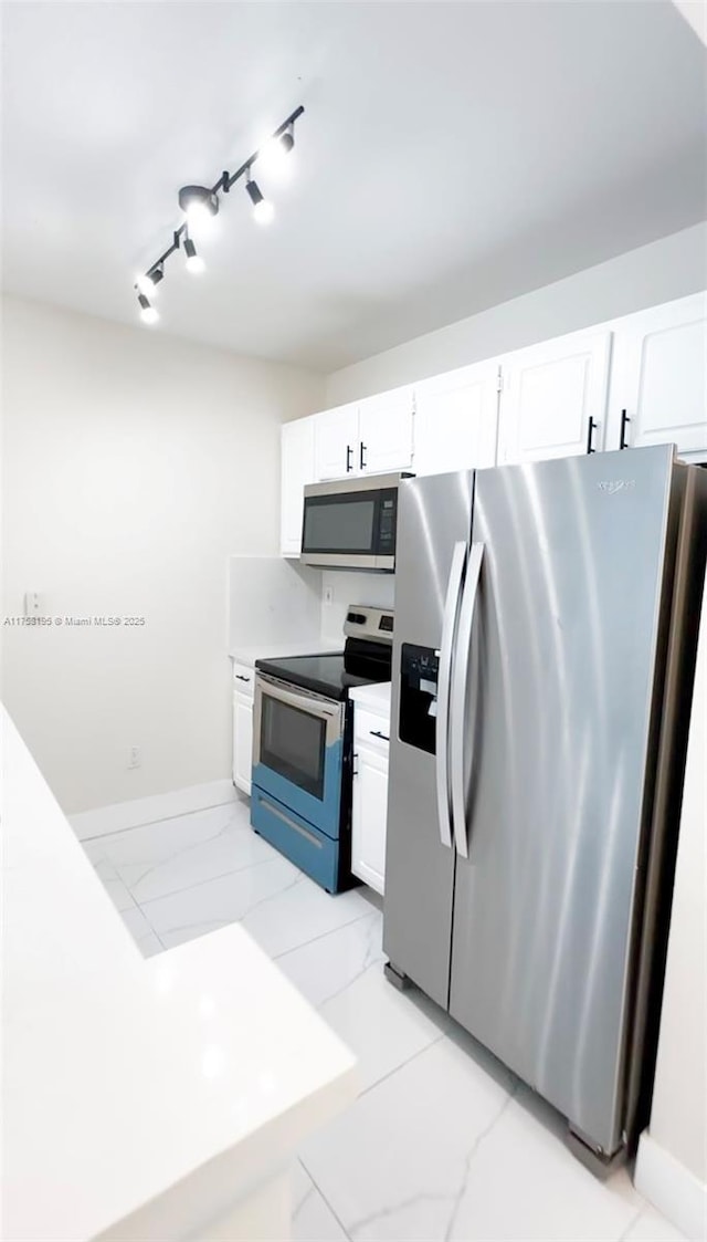 kitchen with marble finish floor, track lighting, white cabinetry, appliances with stainless steel finishes, and baseboards