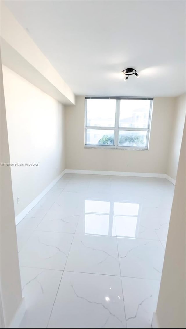 unfurnished room featuring a healthy amount of sunlight, marble finish floor, and baseboards