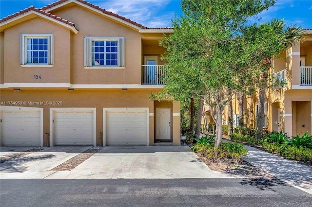 view of property with driveway, an attached garage, a tiled roof, and stucco siding