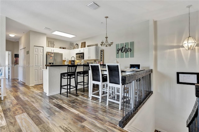 kitchen featuring pendant lighting, stainless steel appliances, visible vents, wood finished floors, and a kitchen bar