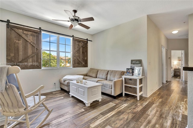 living area featuring a barn door, wood finished floors, a ceiling fan, and baseboards