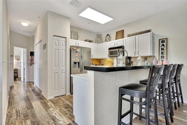 kitchen featuring appliances with stainless steel finishes, light wood-type flooring, a peninsula, and a breakfast bar area