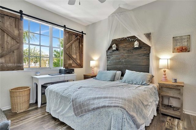 bedroom with ceiling fan, a barn door, wood finished floors, and baseboards