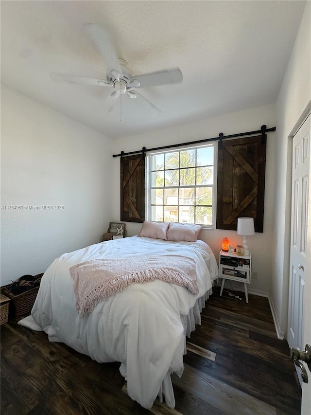 bedroom featuring dark wood-style floors, ceiling fan, baseboards, and a barn door