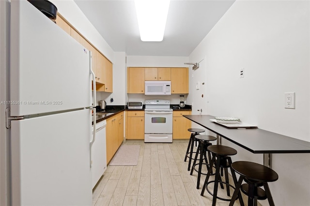 kitchen with white appliances, a toaster, dark countertops, light wood-style floors, and light brown cabinets