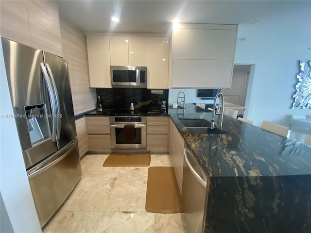 kitchen featuring stainless steel appliances, a peninsula, a sink, dark stone countertops, and modern cabinets